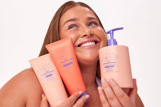 Woman holding three bottles of Luna Bronze tanning products against a white background
